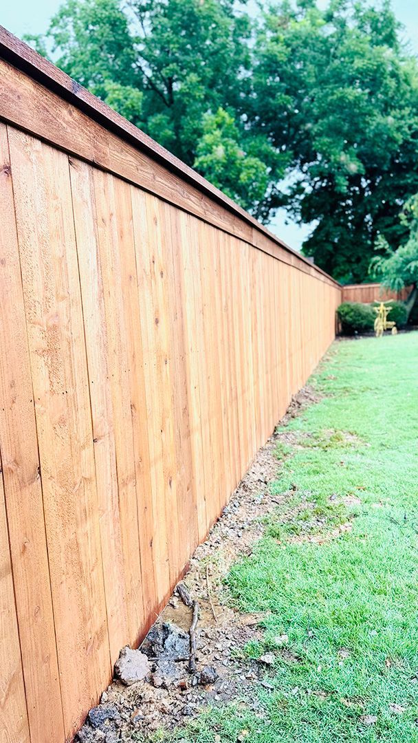Wooden fence in a yard with green grass and trees in the background.