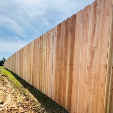 Wooden privacy fence stretches along a grassy area under a blue sky.