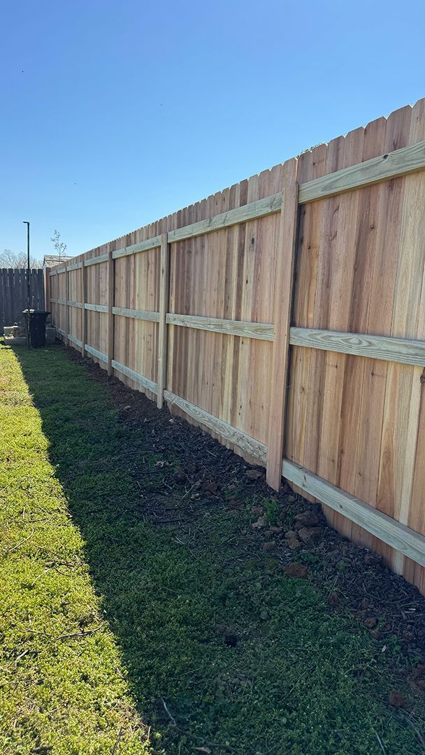 Wooden privacy fence along a green lawn under a clear blue sky.