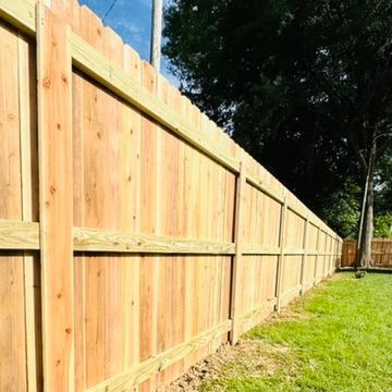 Wooden fence in a yard with green grass, a utility pole, and a partly cloudy sky.