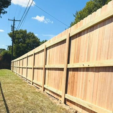 Wooden privacy fence along a grassy lawn, under a blue sky with power lines.