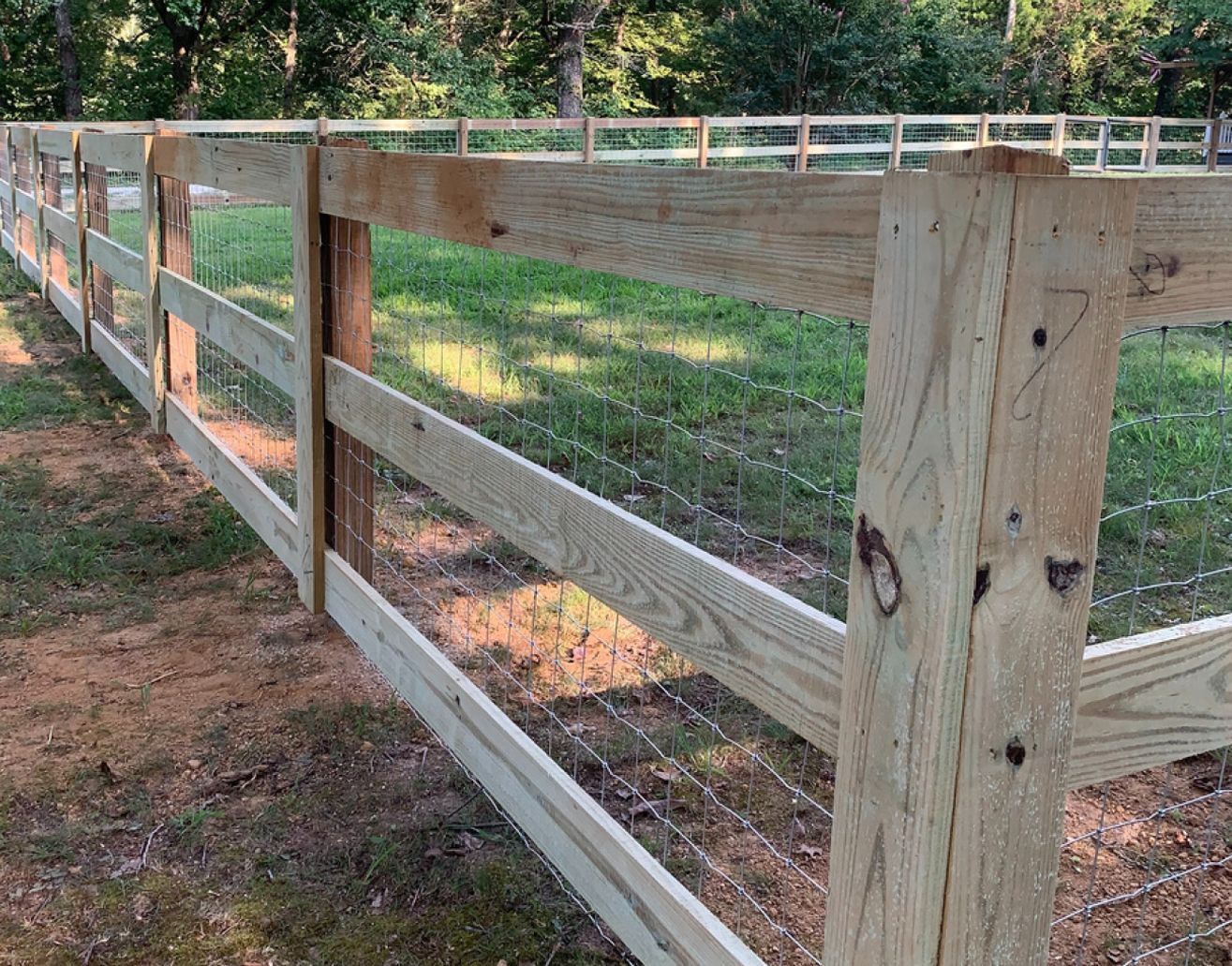 Wooden fence with wire mesh in a grassy field.