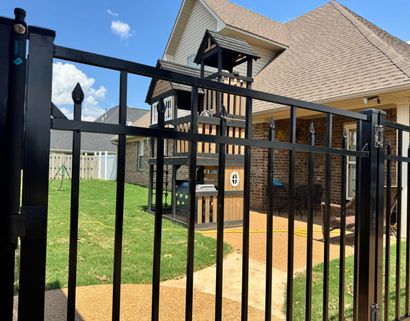 Black metal fence enclosing a backyard with a wooden playset and a house.