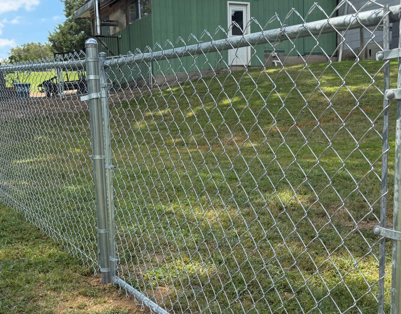 Chain link fence in a grassy yard, with a green building in the background.