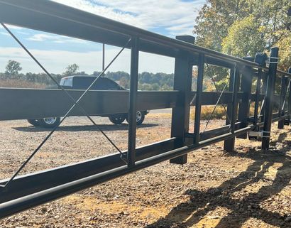 Black metal gate, partially open, with a truck visible in the background. Located outdoors.