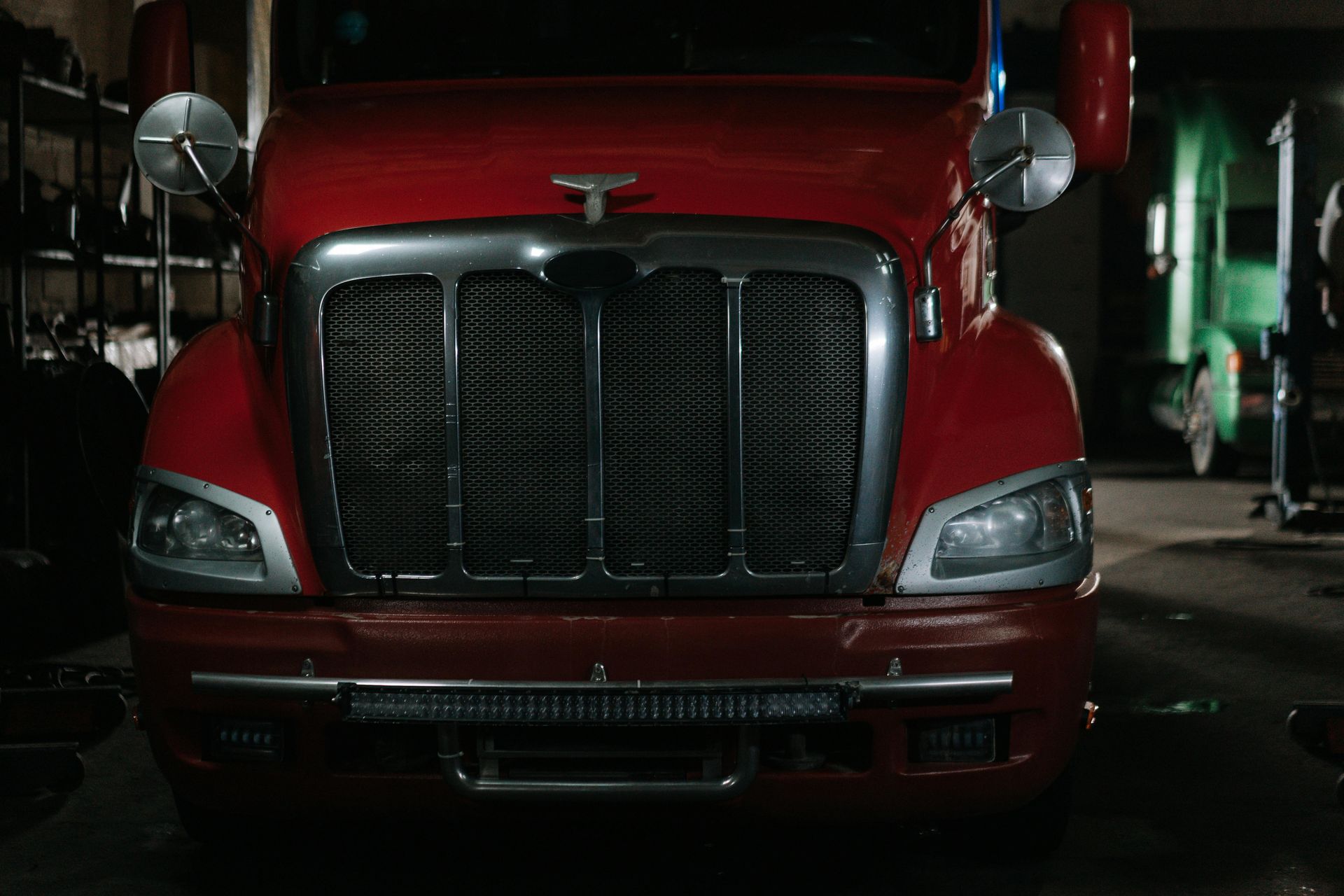 Red semi-truck front in a garage, grill visible, with headlights and a bumper light.