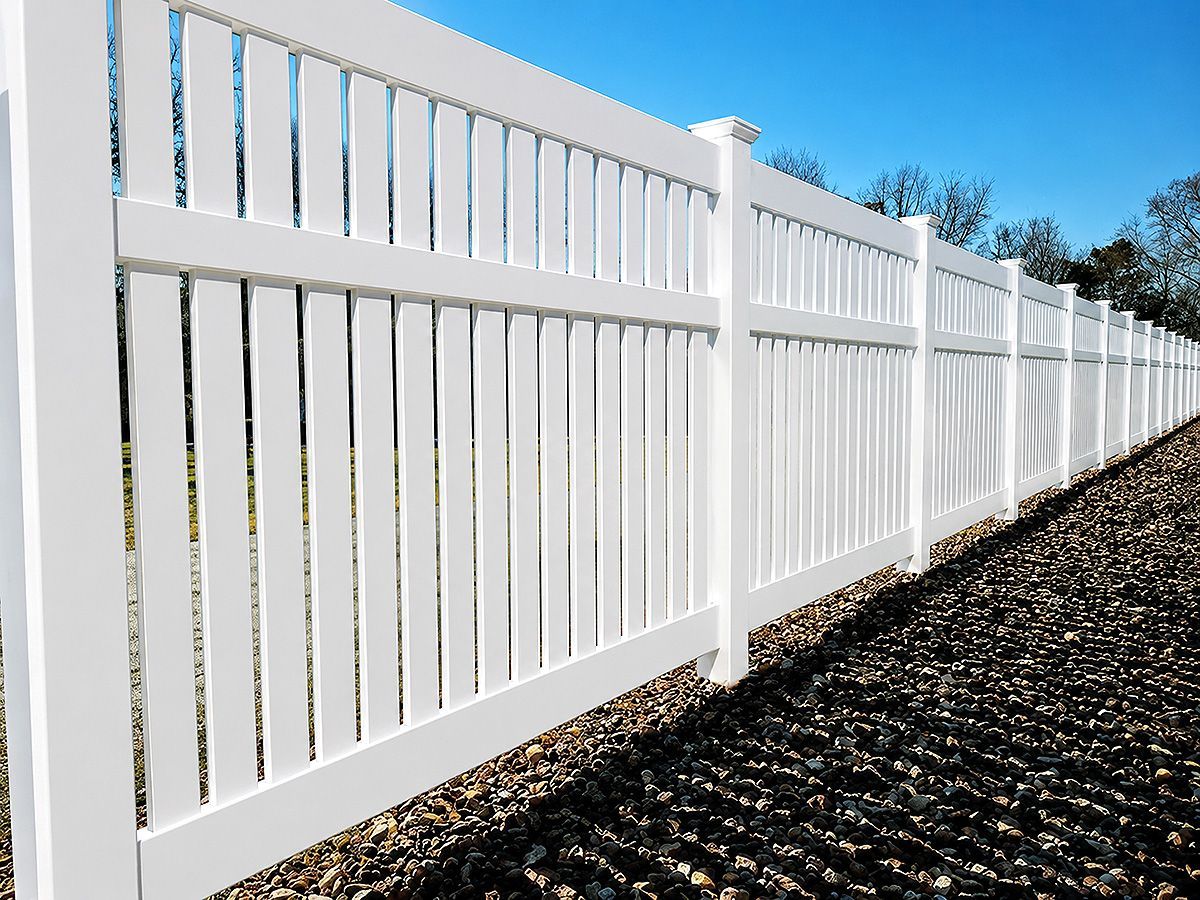 White vinyl privacy fence along a gravel path under a blue sky.