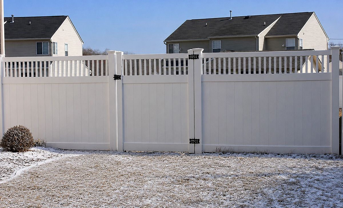 Snowy suburban backyard with a white privacy fence and two houses in the background.
