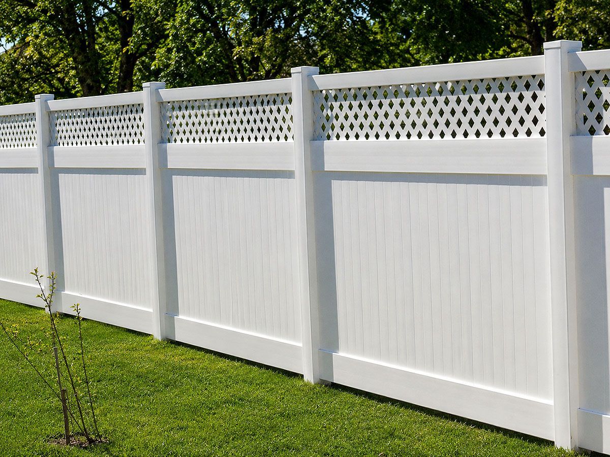 White vinyl privacy fence with lattice top along a green lawn in a yard