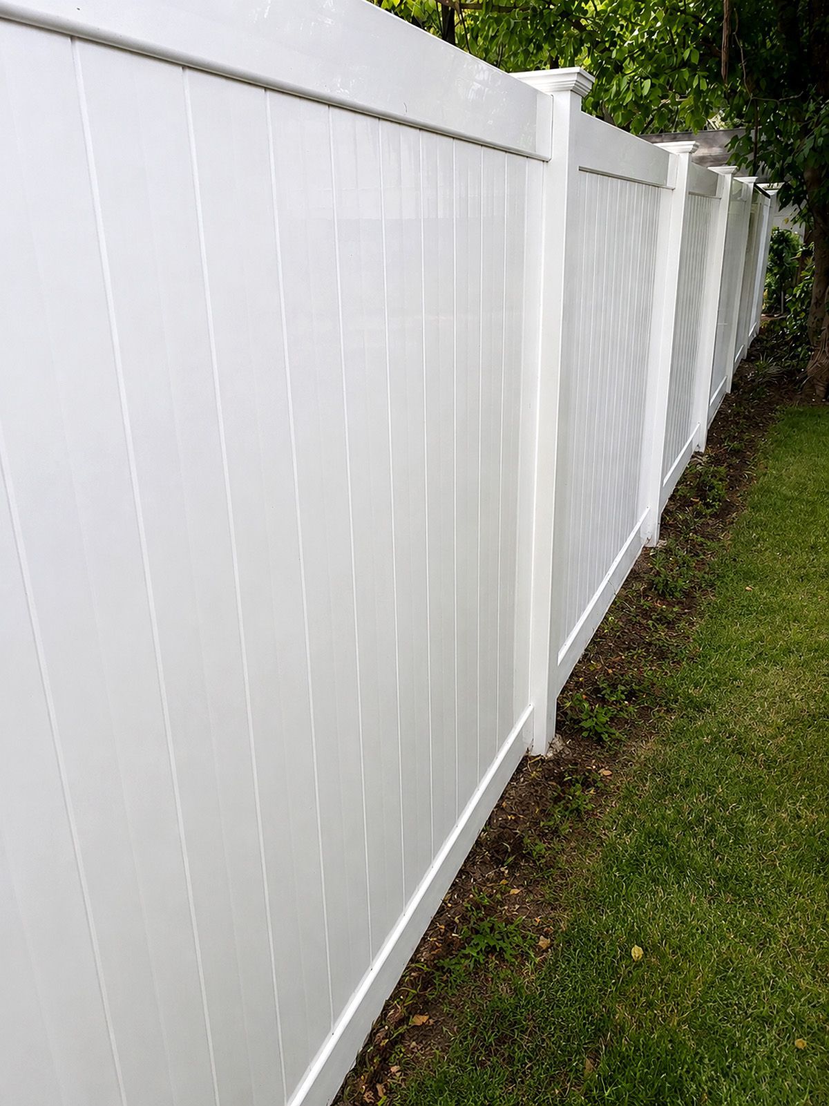 White vinyl fence along a grassy yard with trees in the background