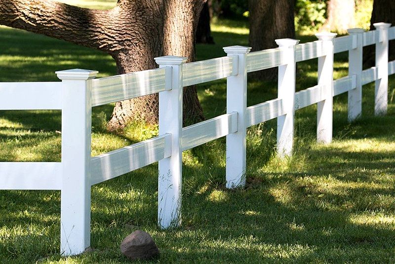 White wooden fence in a sunny grassy yard with trees and shadows