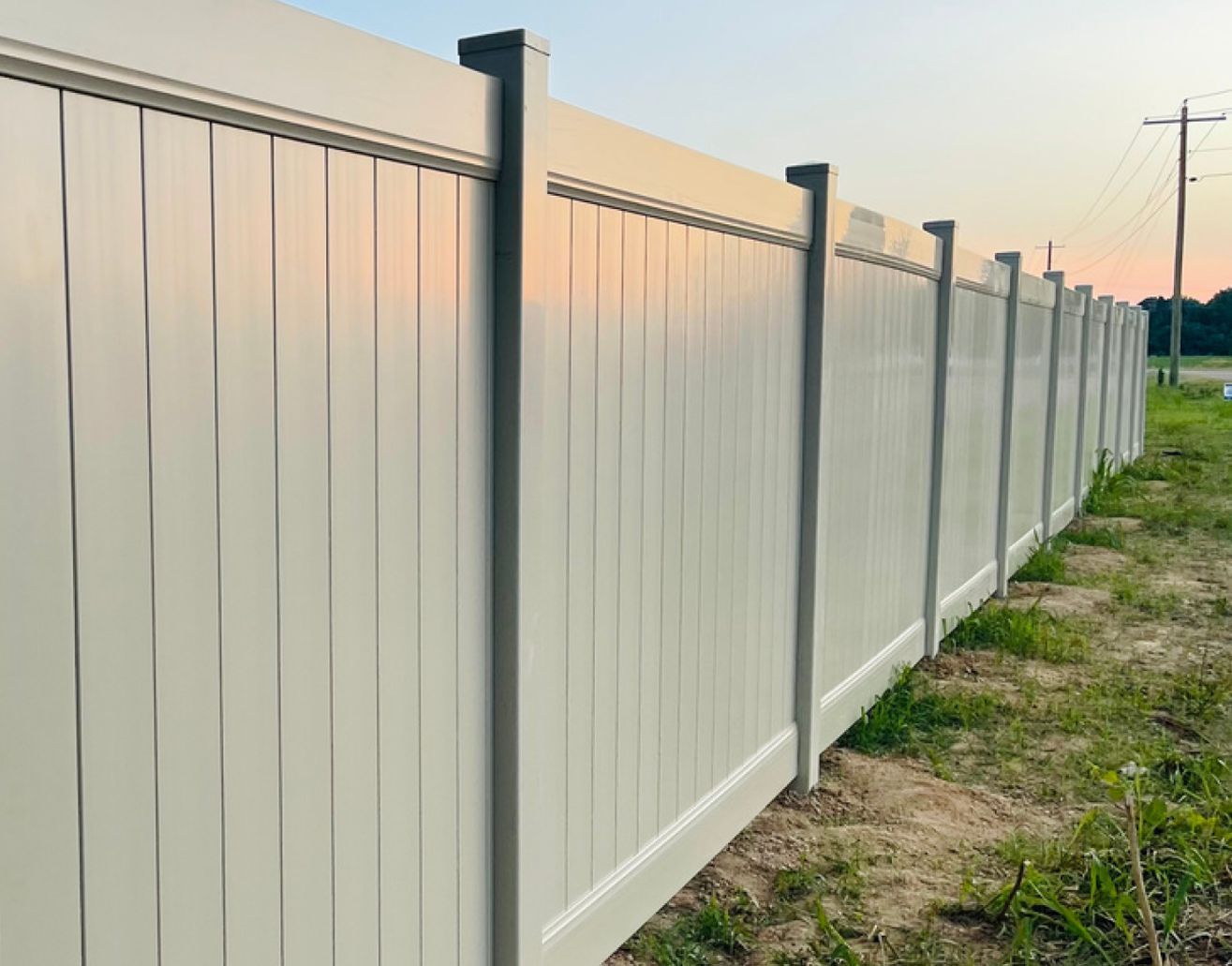 White vinyl fence, tall and extending, with a dusk sky in the background.