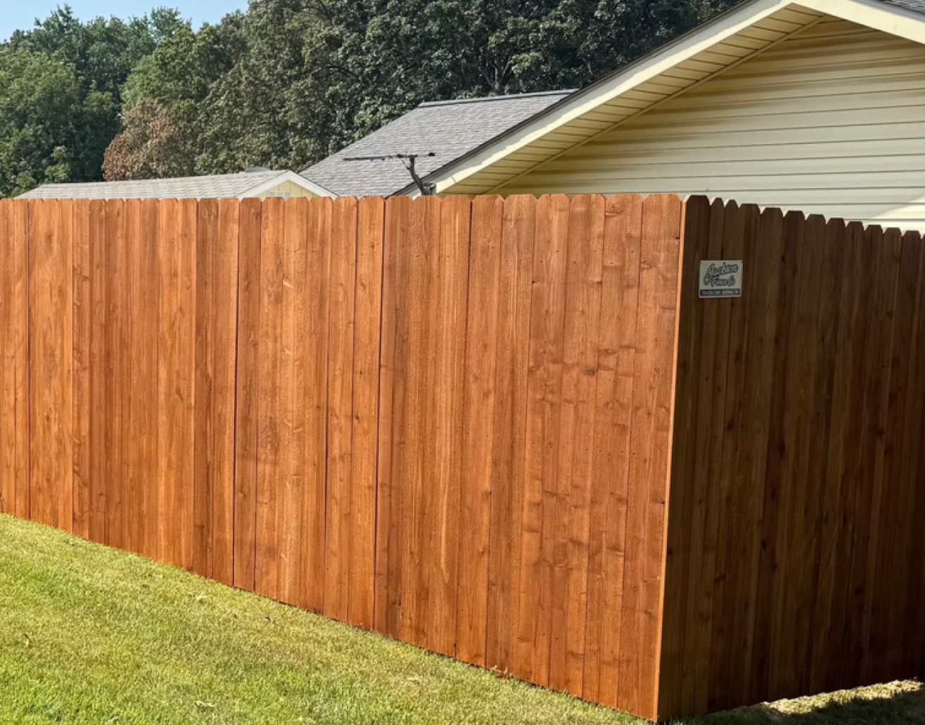 Brown stained wooden fence in a yard next to a light yellow house and green grass.