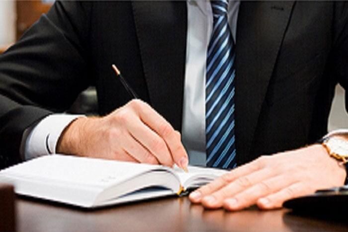 Un hombre con traje y corbata está escribiendo en un cuaderno.
