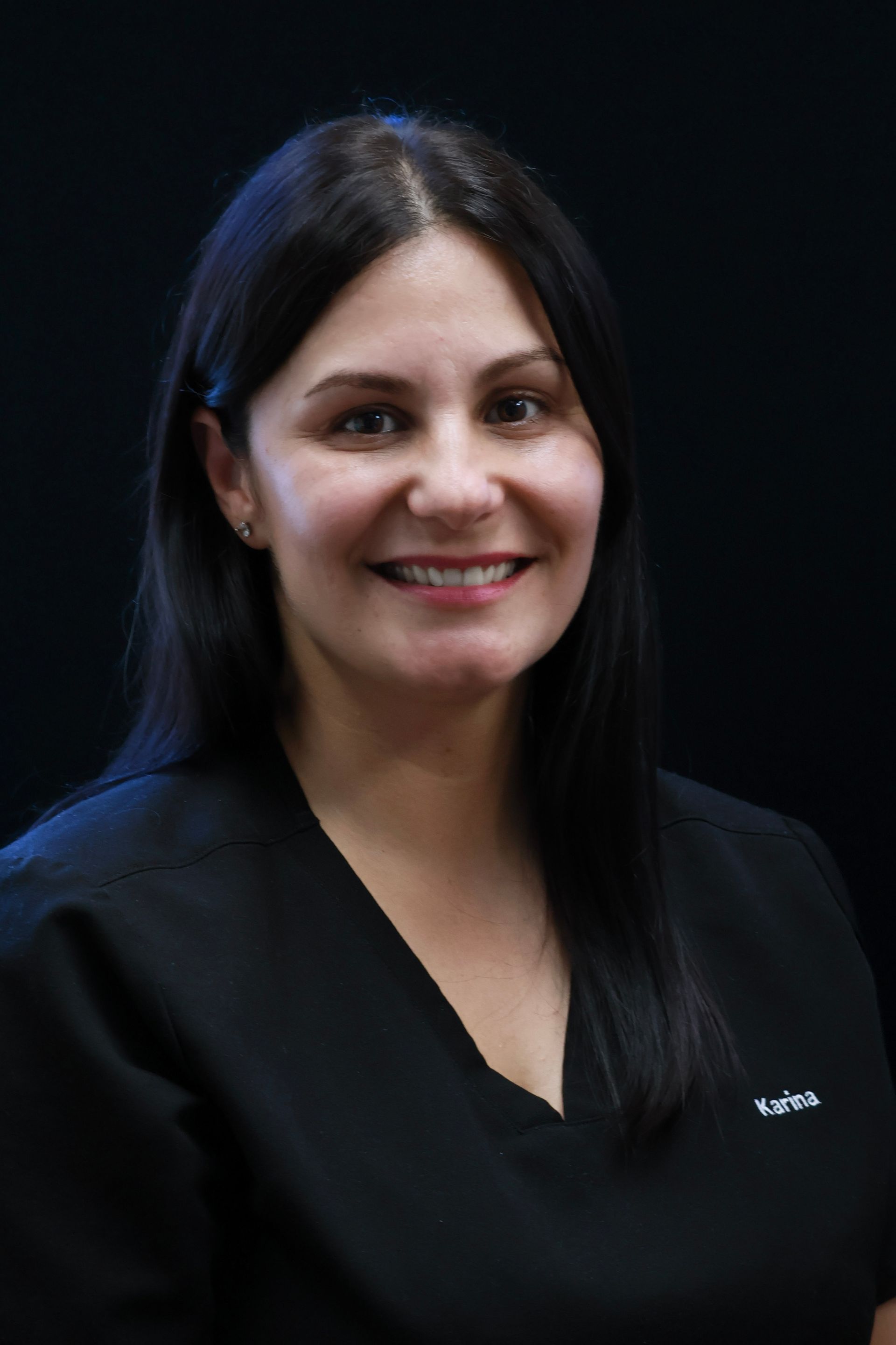 Woman with dark hair, smiling, wearing a black shirt, against a dark background.
