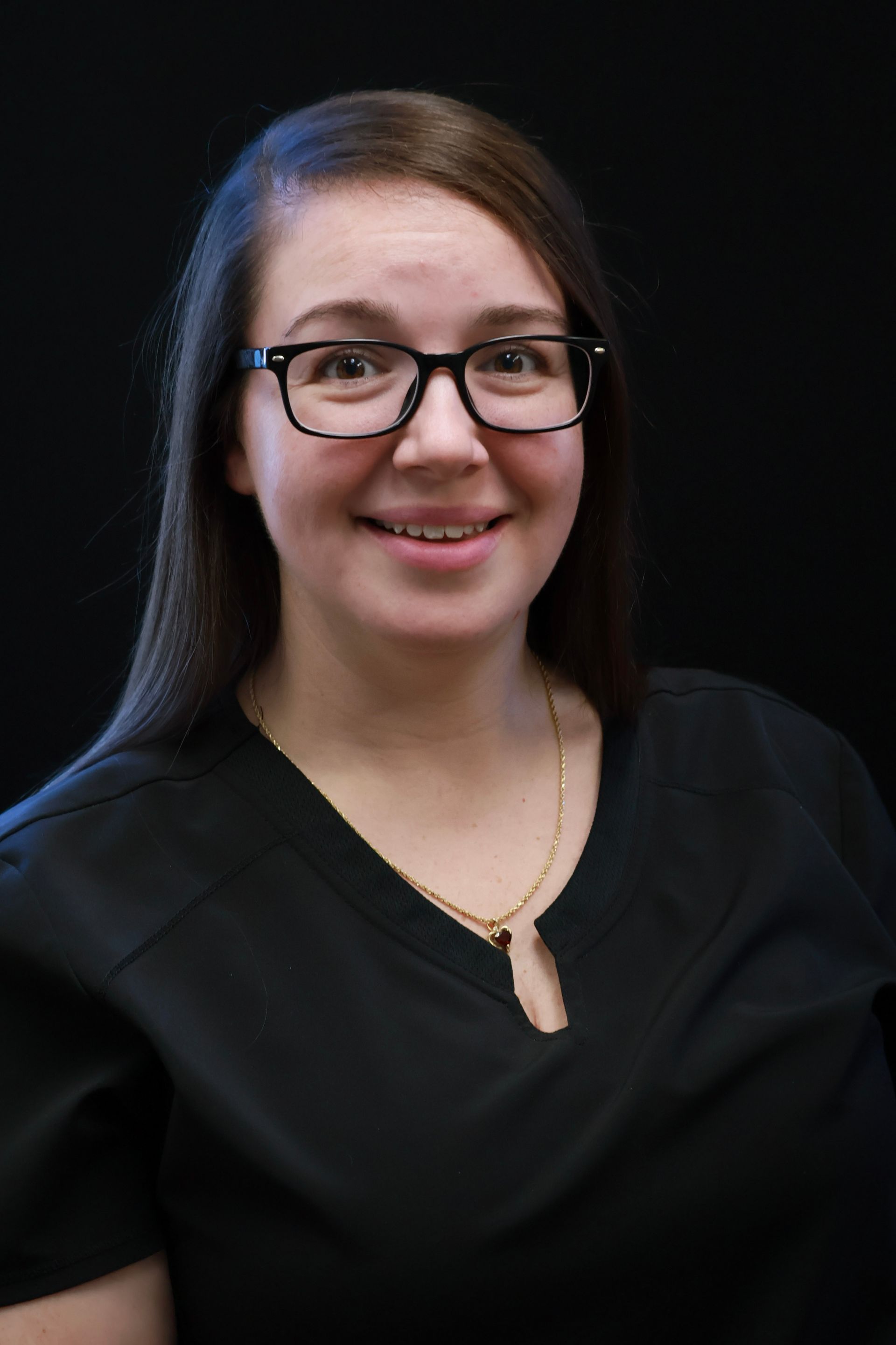 Woman wearing glasses smiles at the camera, black background.