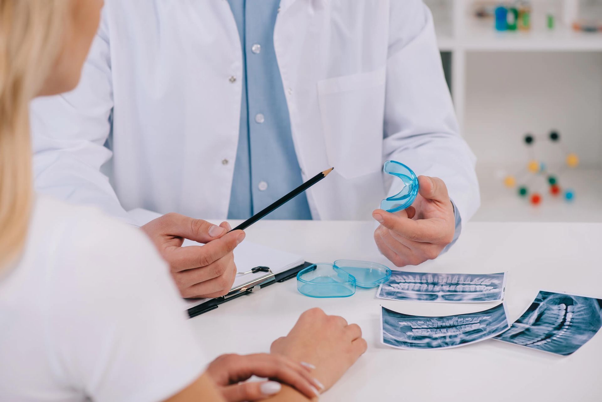 Dentist showing a dental mold to a patient, discussing x-rays at a clinic.