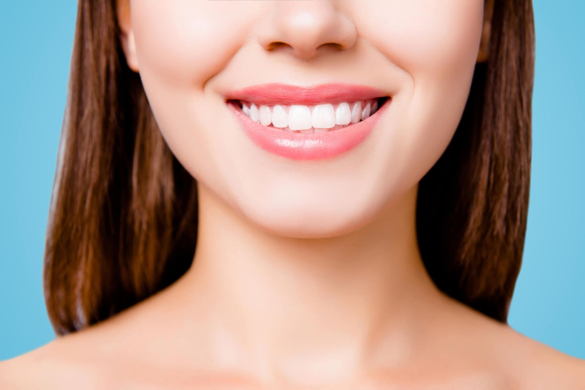 Close-up of a smiling mouth with bright white teeth and pink lips against a blue background.