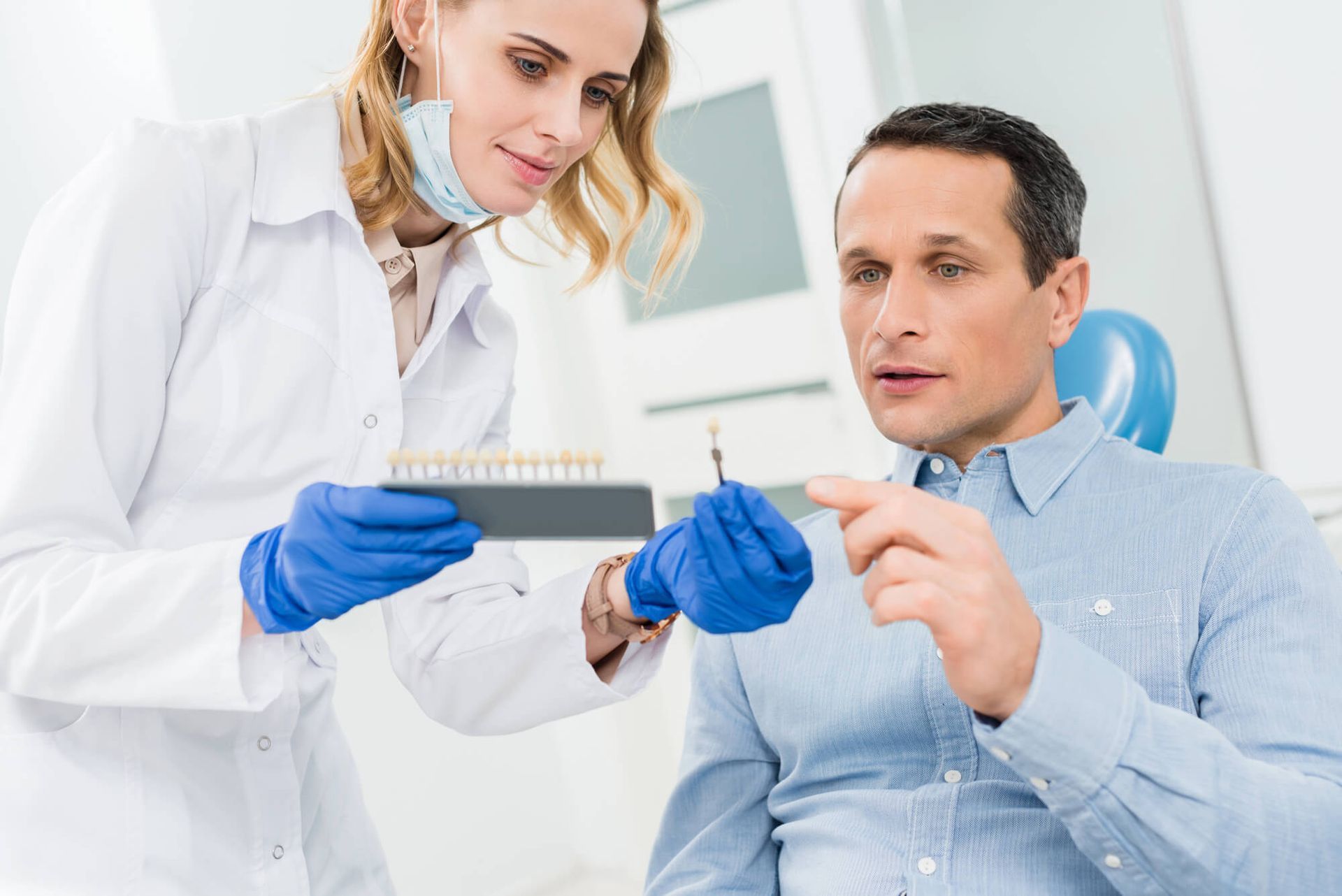 Dentist showing tooth color options to a patient in a dental office; both are holding shade guides.