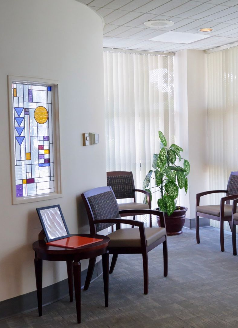 Waiting room with chairs, plant, and stained glass window.