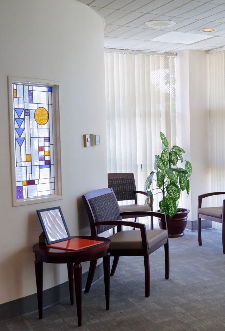 Waiting room with chairs, plant, and stained glass window.
