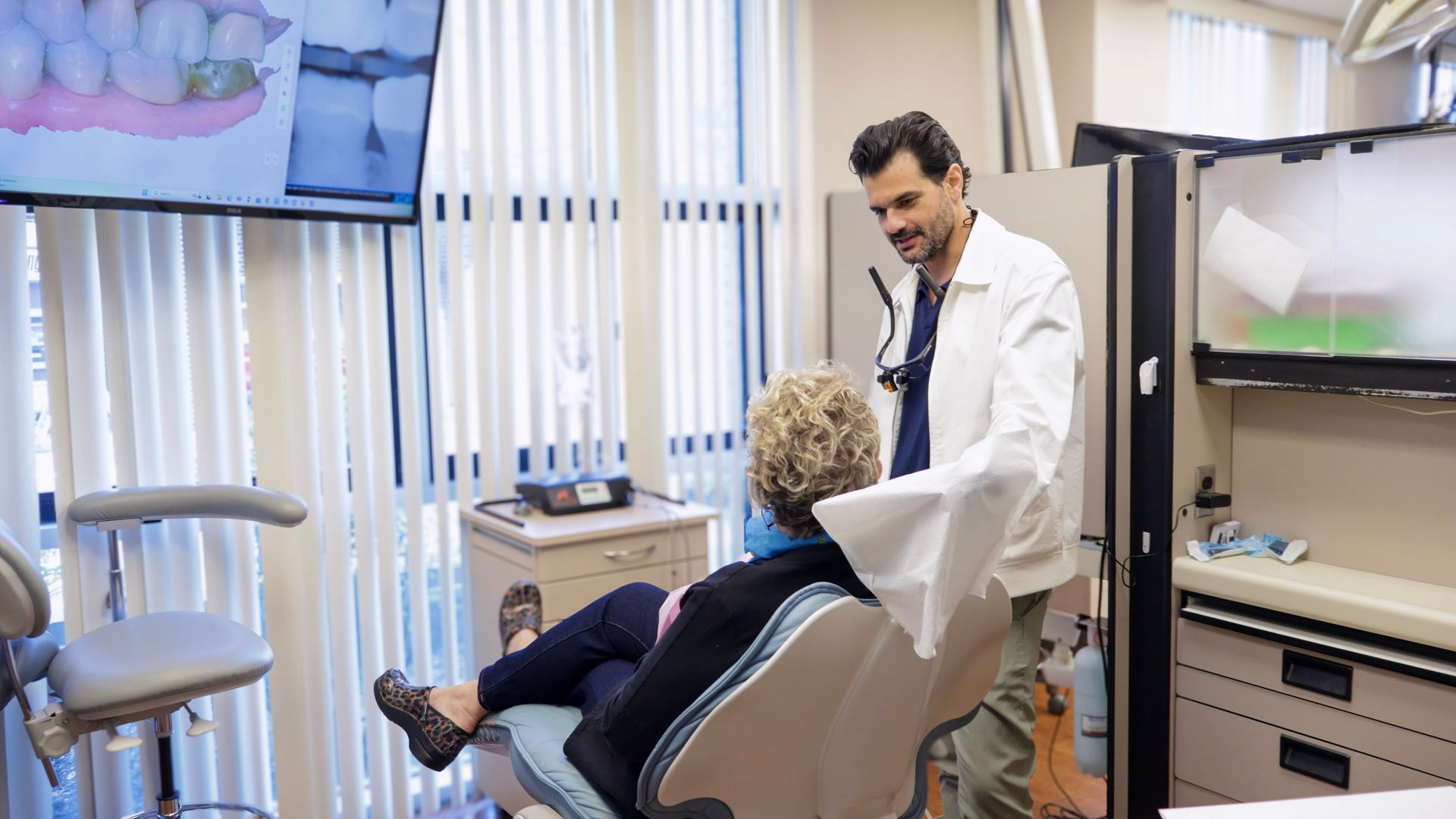 Dentist in white coat explains tooth scan to seated patient in a dental office.