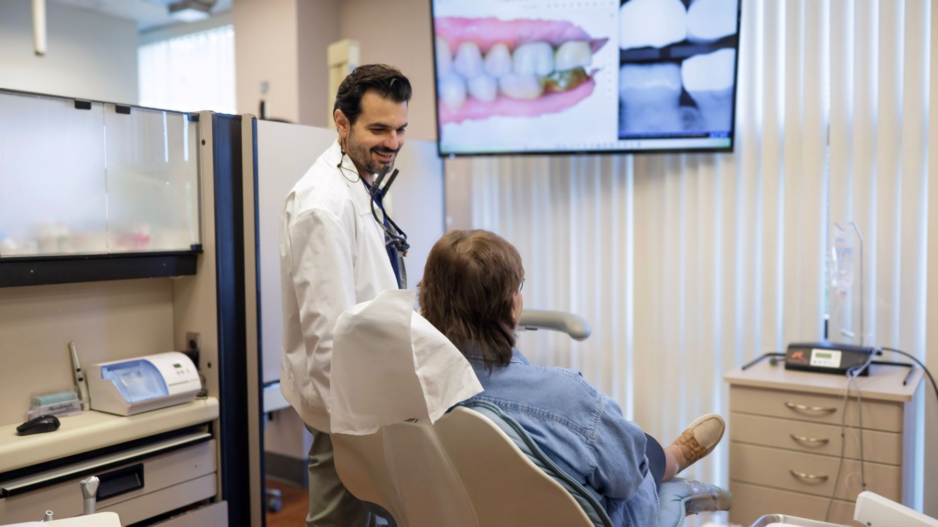 Dentist with patient in dental office, pointing to teeth on screen.