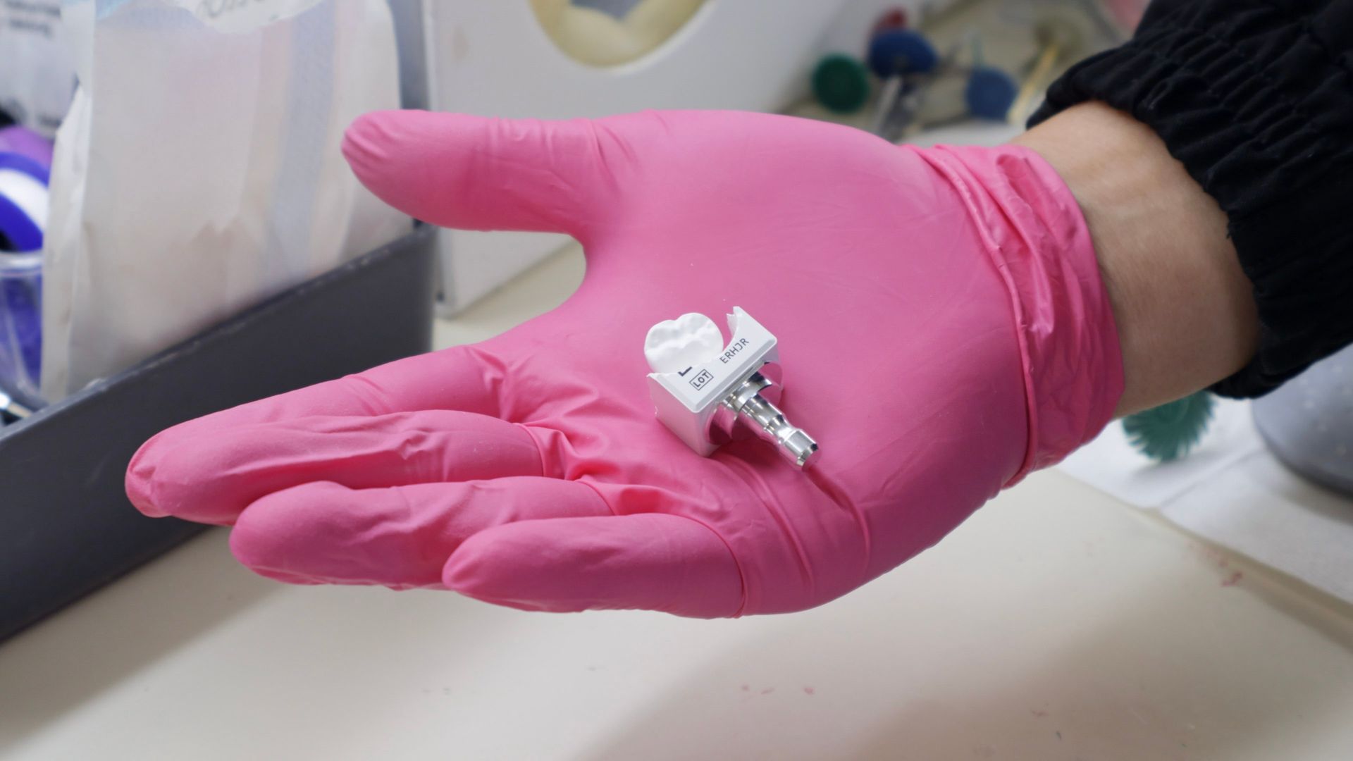 Pink-gloved hand holding a small dental implant component.