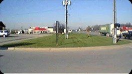 A view of a road with a grass median and a red-roofed building, possibly a restaurant, in the background.