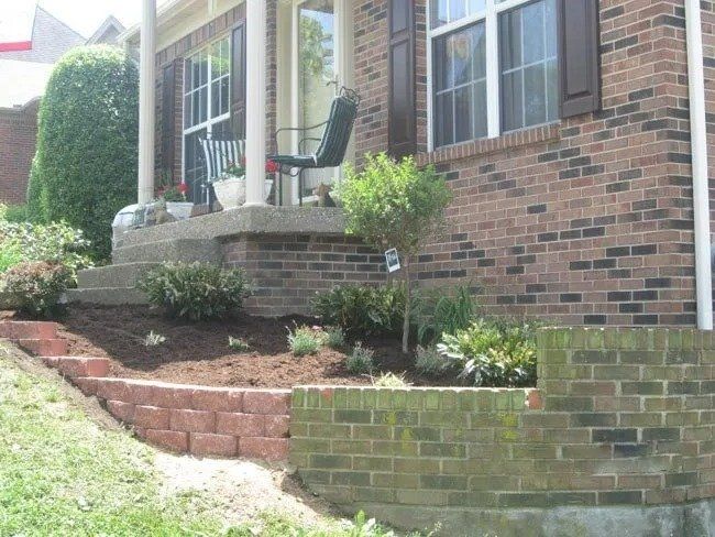 Brick house exterior with a raised porch and landscaped front yard featuring a retaining wall and steps.
