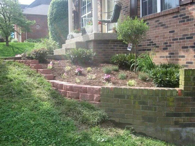 Brick retaining walls with a landscaped yard leading up to a house with a porch and columns.