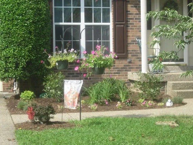 A well-landscaped front yard with a brick home, window boxes with pink flowers, and a welcome flag.