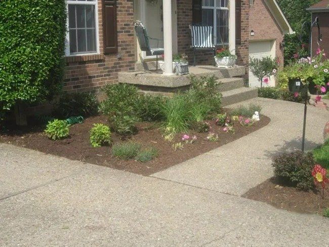 A brick house with a small garden bed by the front steps. The garden has plants and mulch.