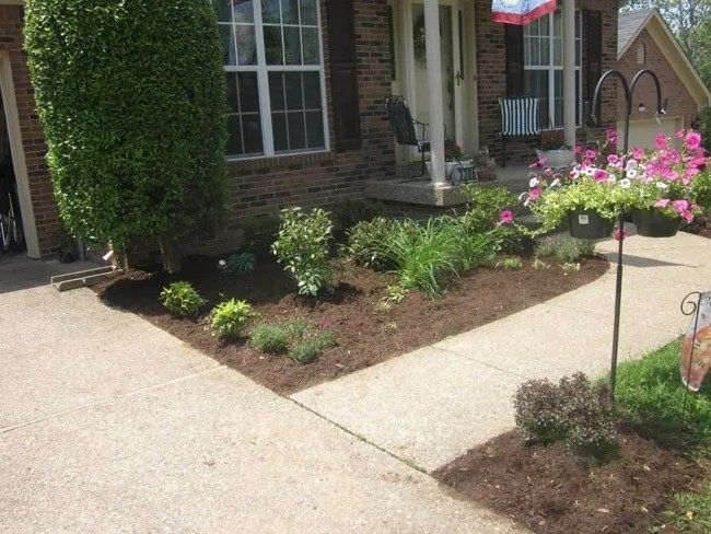 Well-maintained front yard with a walkway, flower beds with mulch, and a hanging basket of pink flowers.