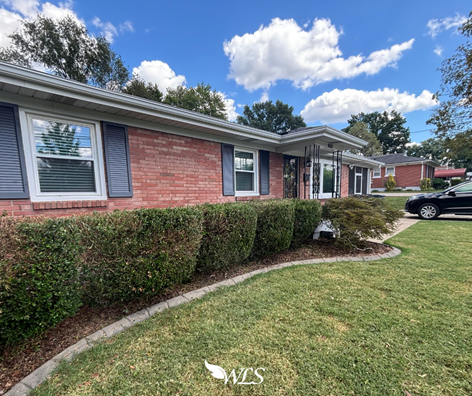Brick house with neatly trimmed bushes and green lawn under a blue sky.
