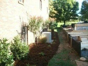 A residential building with a row of newly planted shrubs and mulch alongside the wall. A grassy area is next to the planting.