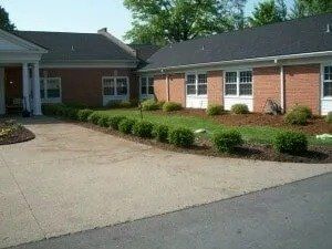 Exterior view of a brick building with a driveway, green bushes, and a manicured lawn.