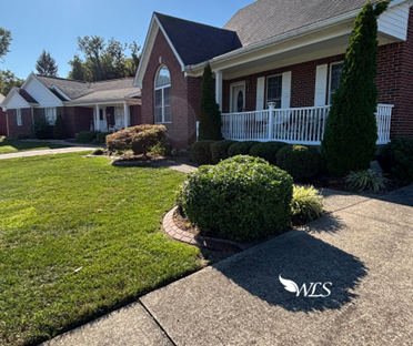 Brick house with green lawn, bushes, and walkway. Sunny day.