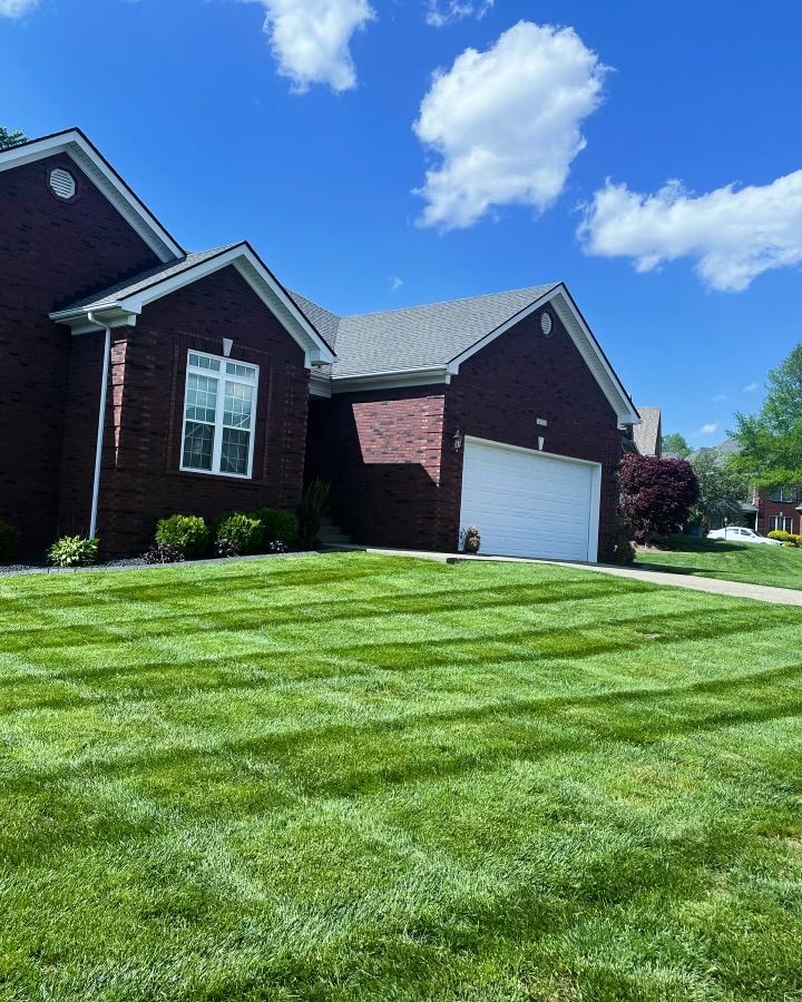 A brick house with a well-manicured lawn featuring lawn stripes, blue sky, and white clouds.