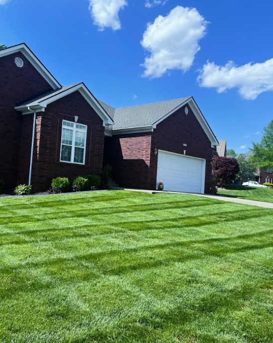 A Brick House with a White Garage Door and a Lush Green Lawn in front of it – Louisville, KY – Wayne's Lawn Service