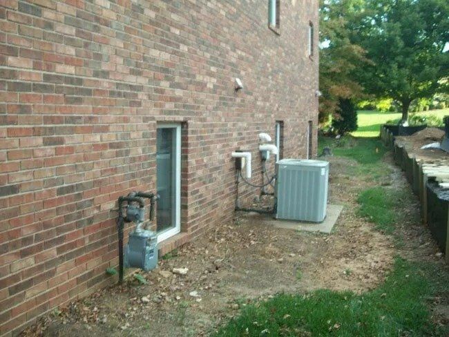 Brick building exterior with an air conditioning unit and gas meter. Bare earth ground and some grass.