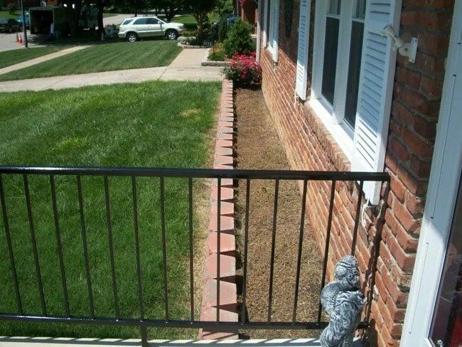 Black railing in front of a brick building, bordering a grassy lawn and mulch bed. A bird statue sits at the base.