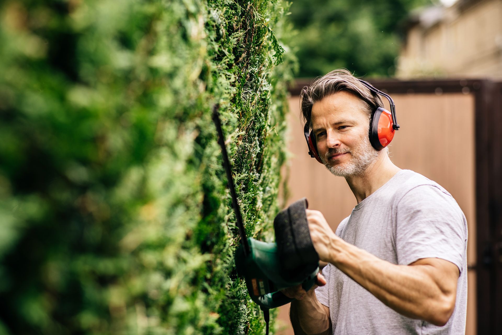 A landscaper trimming a hedge with an electric trimmer.