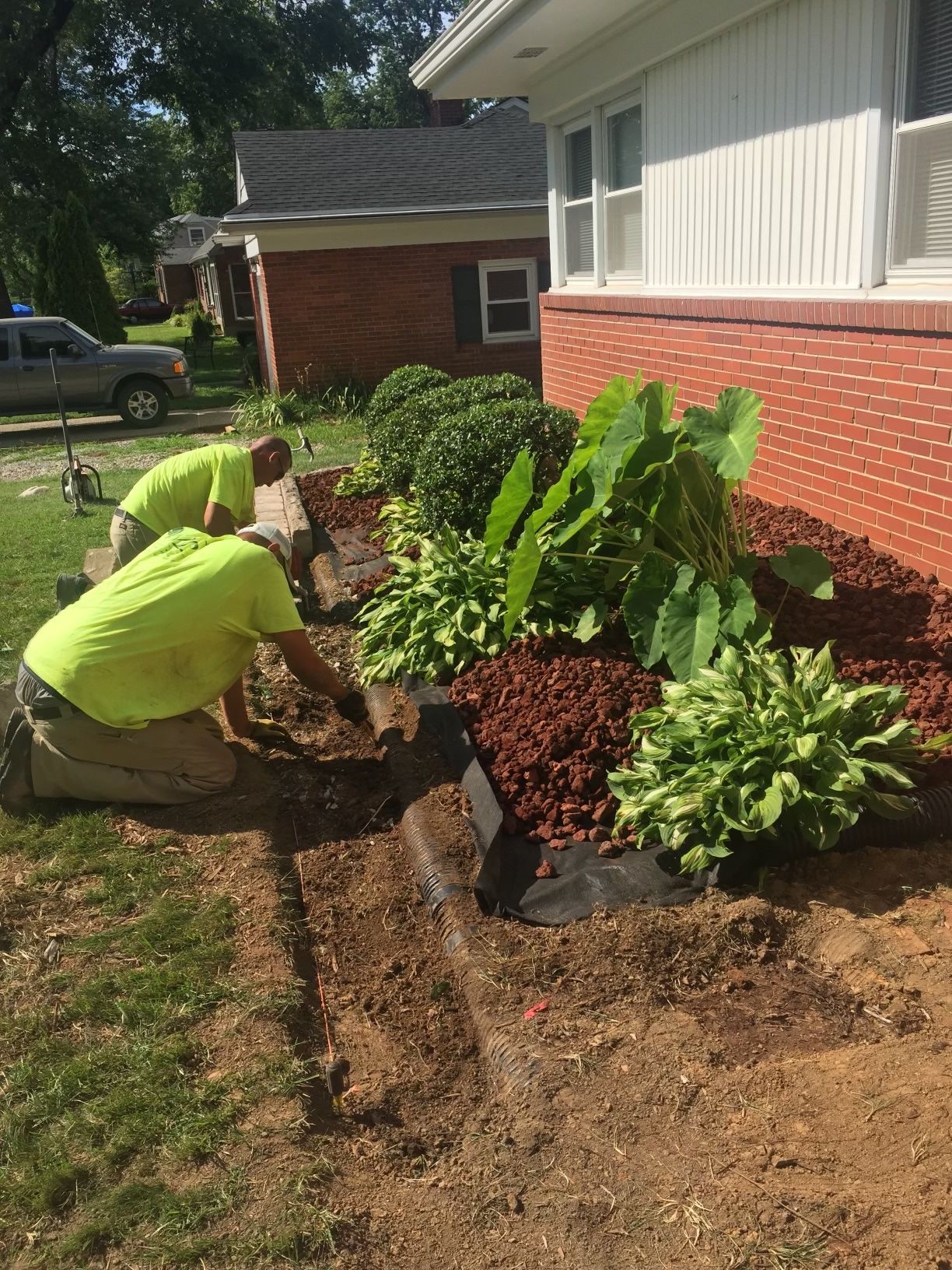 Two Men are Working in a Garden in Front of a Brick House – Louisville, KY – Wayne's Lawn Service