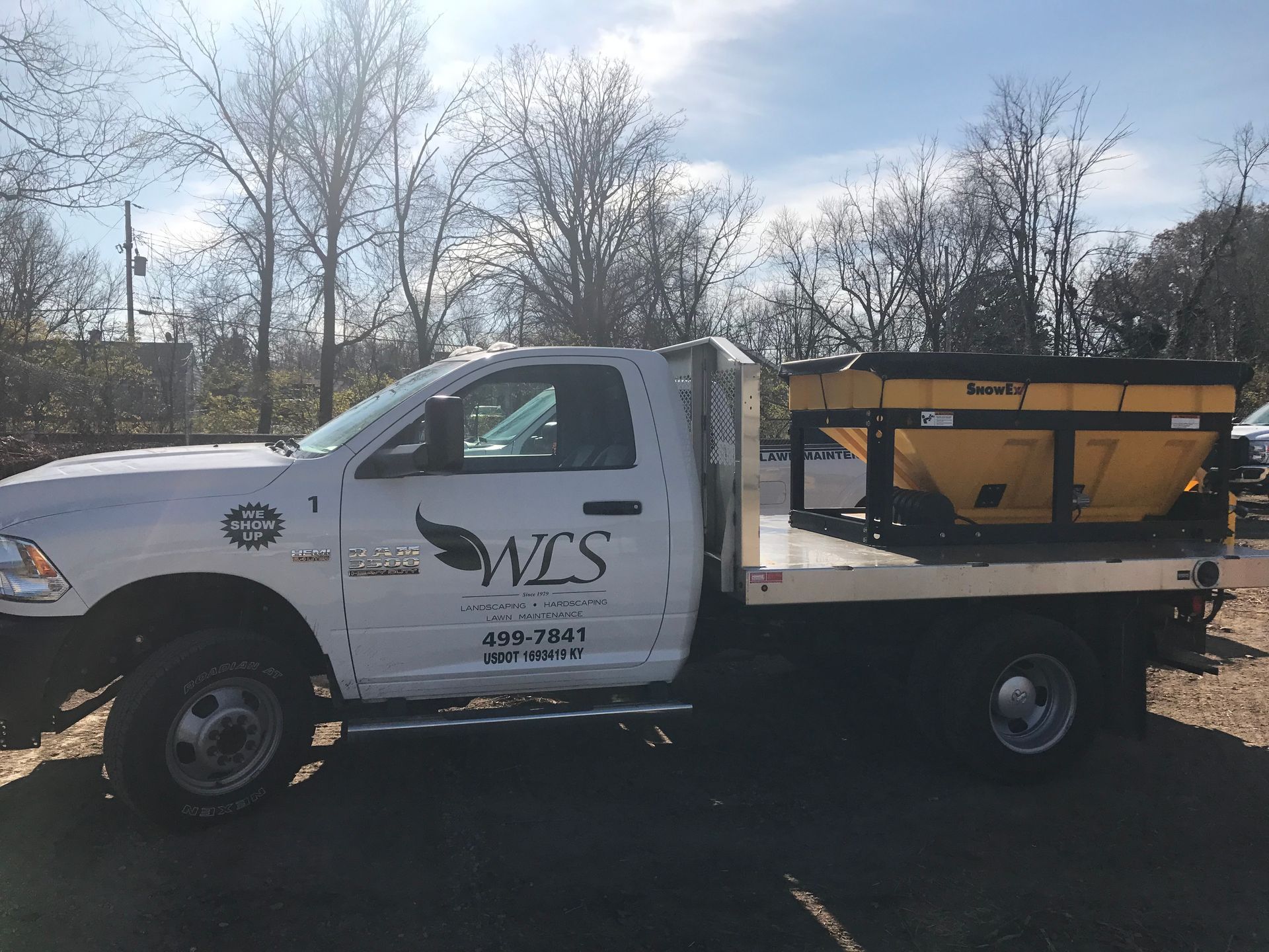 White work truck with a flatbed and yellow salt spreader; WCS logo on the side.