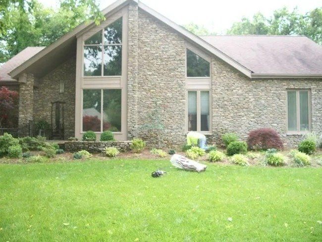 A stone-faced house with a manicured lawn; a person tends to the landscaping.