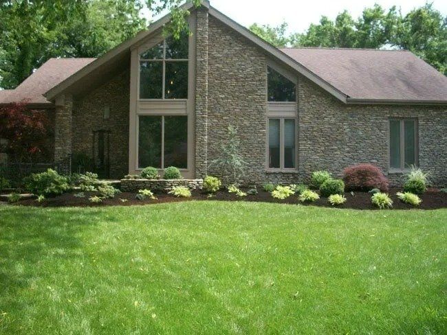 House with brick exterior, large windows, and well-manicured lawn and garden.