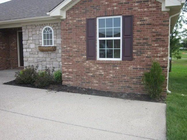 House exterior with brick and stone facade, window with dark brown shutters, and a concrete driveway.