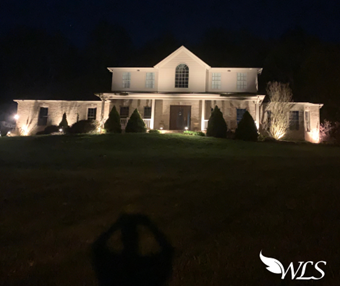 House at night, illuminated by landscape lighting. Dark lawn, stone facade, and arched window.