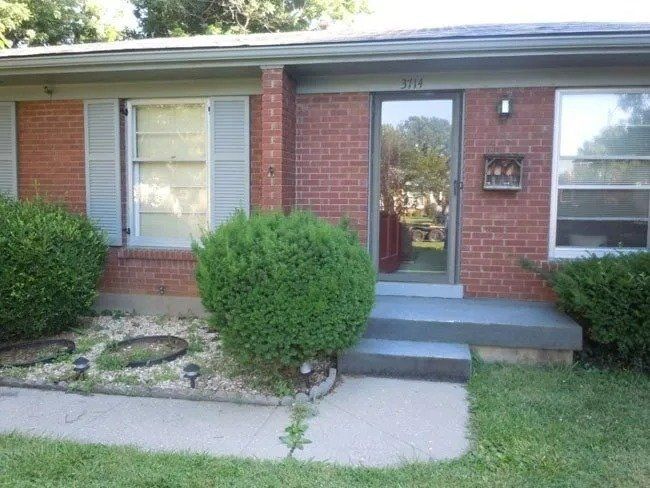 Brick house with a front door and two windows, a small front yard, and shrubs.
